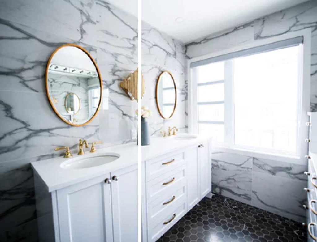 a bathroom with double vanity area that has round gold framed mirrors, white countertop and cabinet drawers, gold faucets and accent decorations against the marble-tiled walls and black flooring