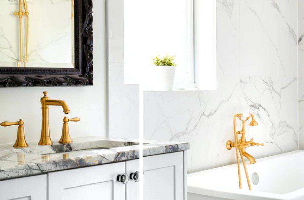 a bathroom with gold faucets, gray countertop over the white cabinets, and a white tub against the marble walls