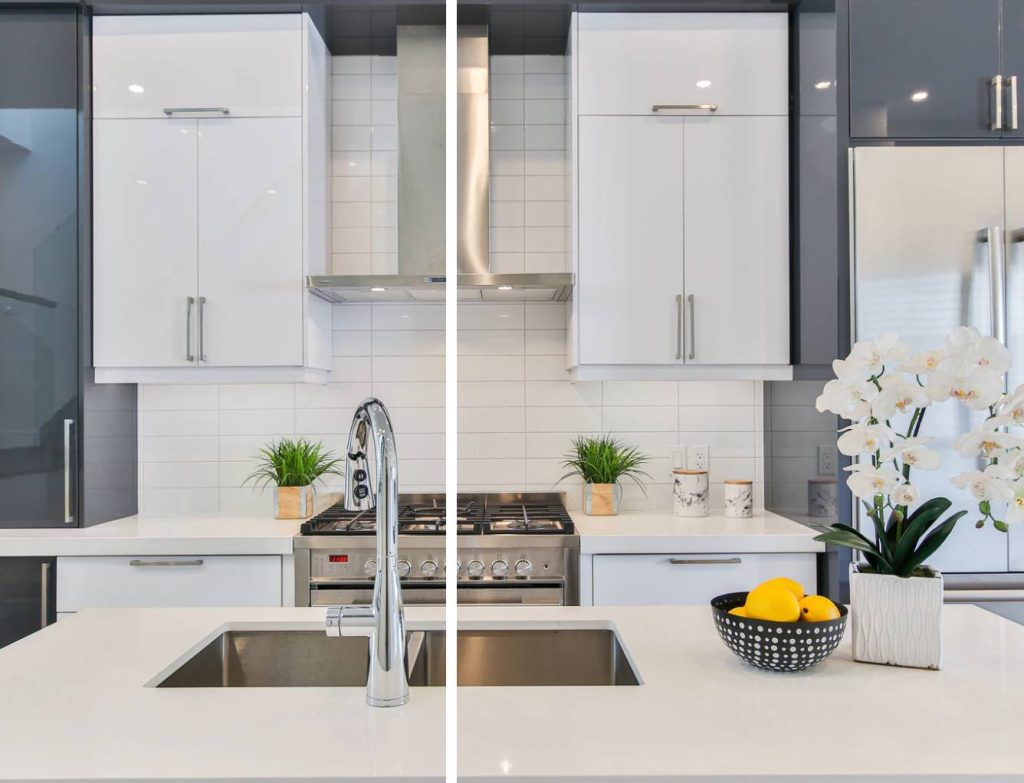 a simple kitchen with white glossy cabinets, white tiled backsplash, and white countertops and kitchen island that has a flower decoration and lemons on top
