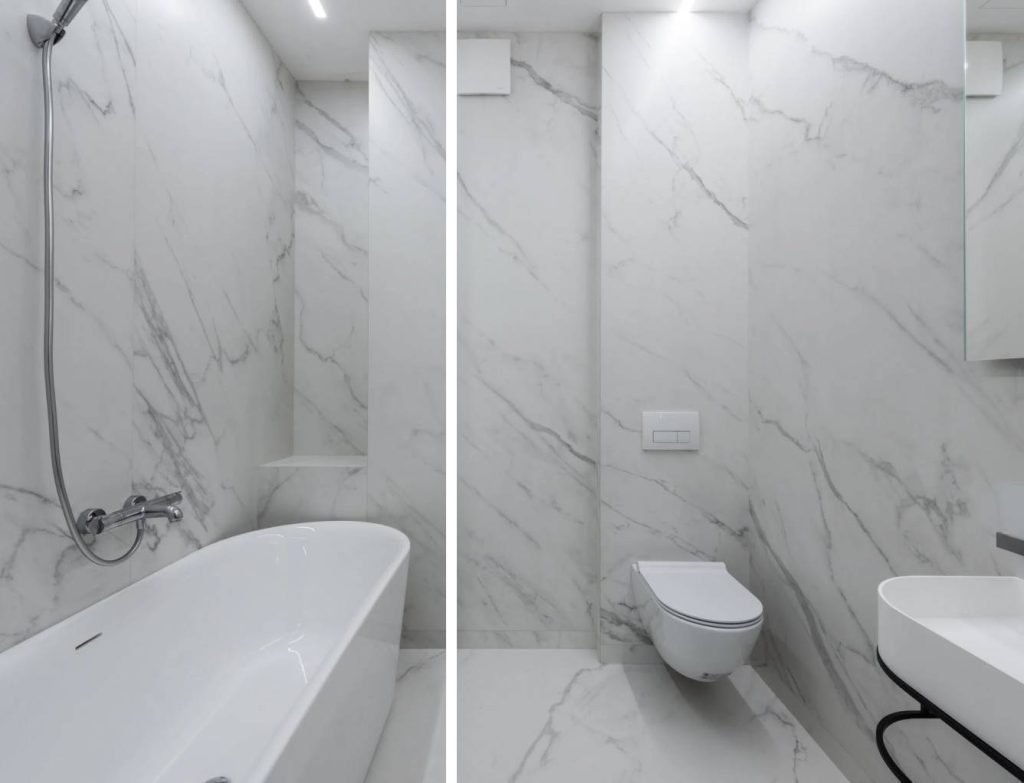 a floor to ceiling marble bathroom with white hanging toilet bowl, a sink, and a bathtub with a shower head