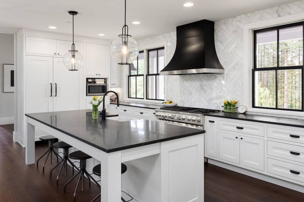 a black and white kitchen with black countertop, kitchen island, chairs, and other details such as lights and walls over the dominant white walls and cabinets
