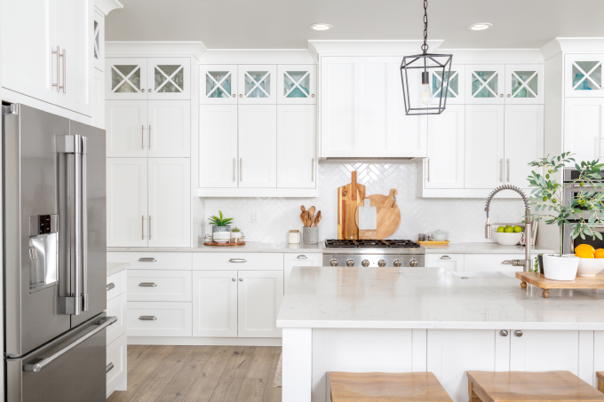 white kitchen with minimalist white cabinets and kitchen island with stainless two-door refrigerator and stove