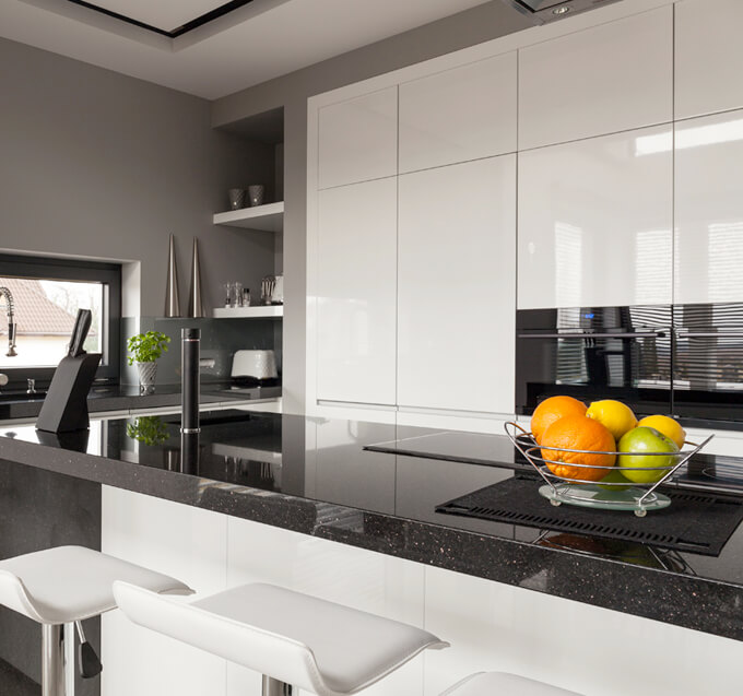 a modern kitchen with black countertops, white cabinets, black kitchen islands, and white bar stool chairs