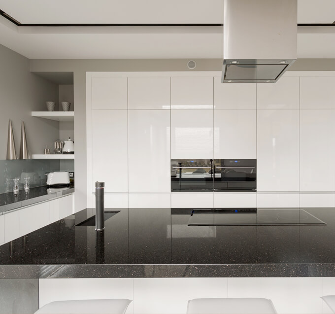 a modern kitchen with handleless cabinets, a black countertop, and a kitchen island with a built-in burner and faucet